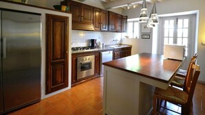 A kitchen with wooden cabinets, a stainless steel refrigerator, a stove, and a dishwasher. There is a large island with chairs.