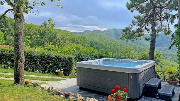 A hot tub on a stone patio with a view of green hills.