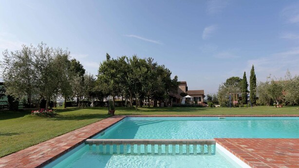 Une piscine rectangulaire bordée de briques, entourée d’une pelouse bien entretenue et d’arbres.