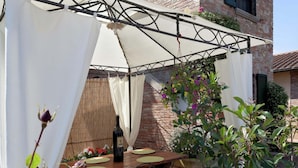 Une terrasse extérieure avec une table et des chaises, une bouteille de vin et une structure en forme de pergola.