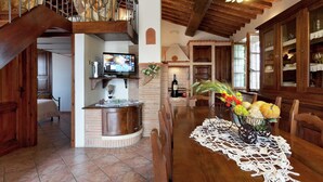 Une cuisine spacieuse avec un escalier en bois, un coin repas avec une table dressée pour deux personnes, et un téléviseur fixé à un mur en briques.