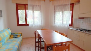 A compact kitchen with a dining table and chairs, a sofa, and a window with curtains. - Belvilla by OYO Elios Trilo Due (Rosolina)
