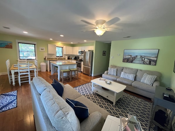 A modern living room with a grey sofa, a coffee table, and a dining area with white chairs.