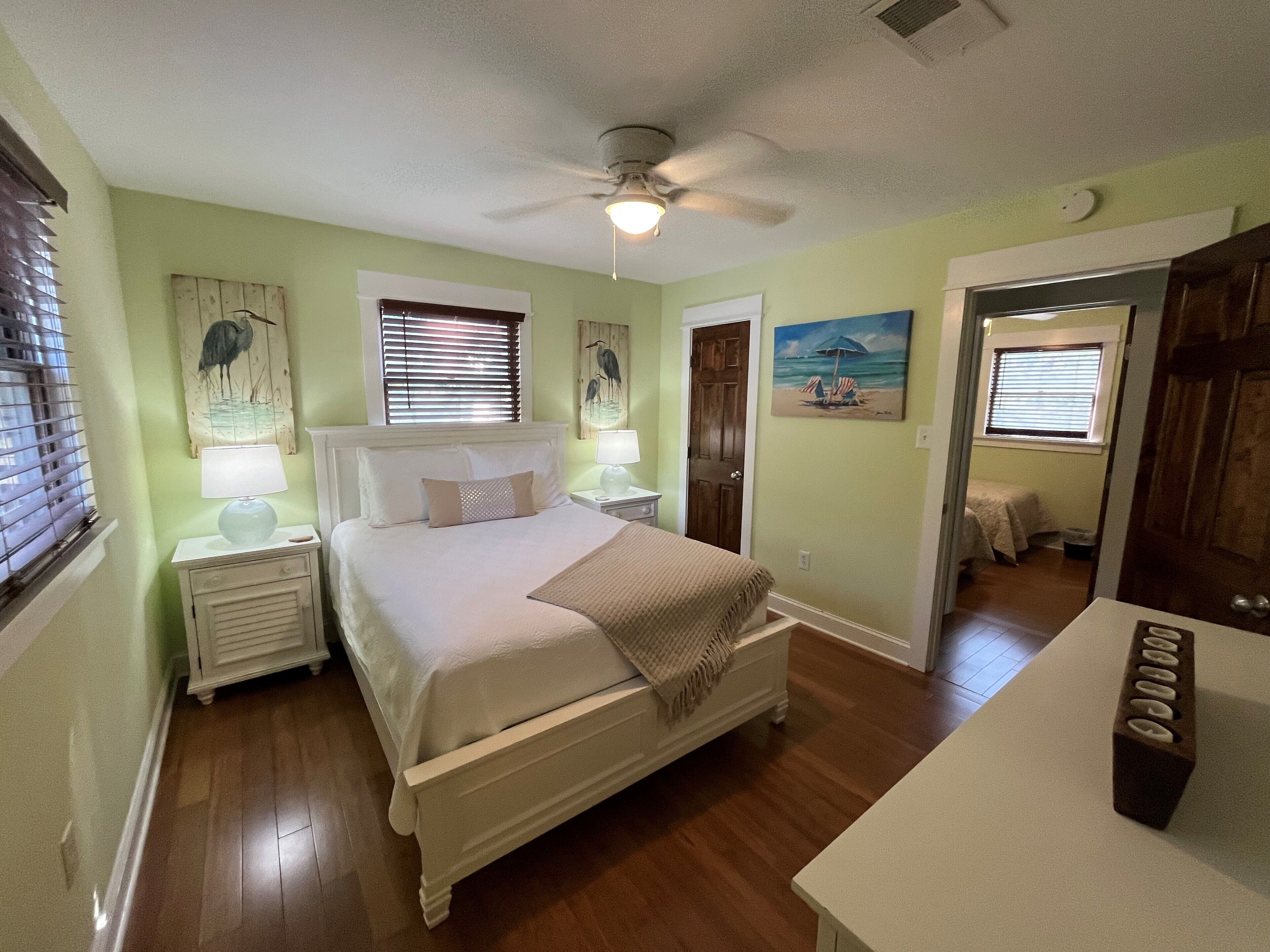 A bedroom with a bed, bedside tables, a ceiling fan, and artwork on the walls.