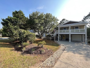A two-story house with a garage, surrounded by trees and a well-maintained lawn. - Swept Away One -Great Family Beach Home (Kill Devil Hills)