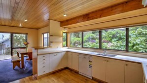 A modern kitchen with wooden cabinets, a built-in dishwasher, and large windows offering a view of a lush garden.