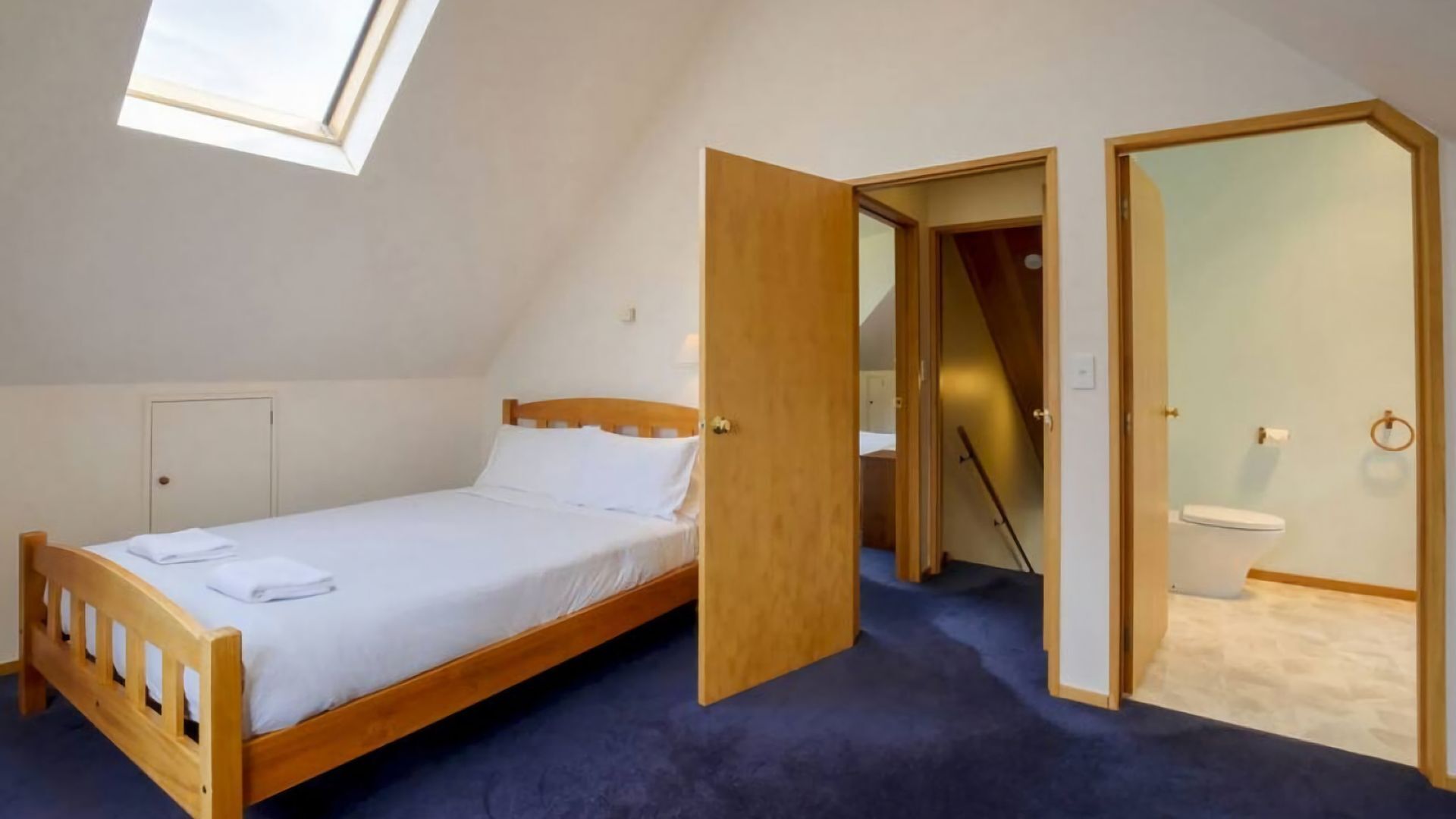 Un dormitorio con una cama individual, una puerta de madera y un baño visible a través de una puerta abierta.