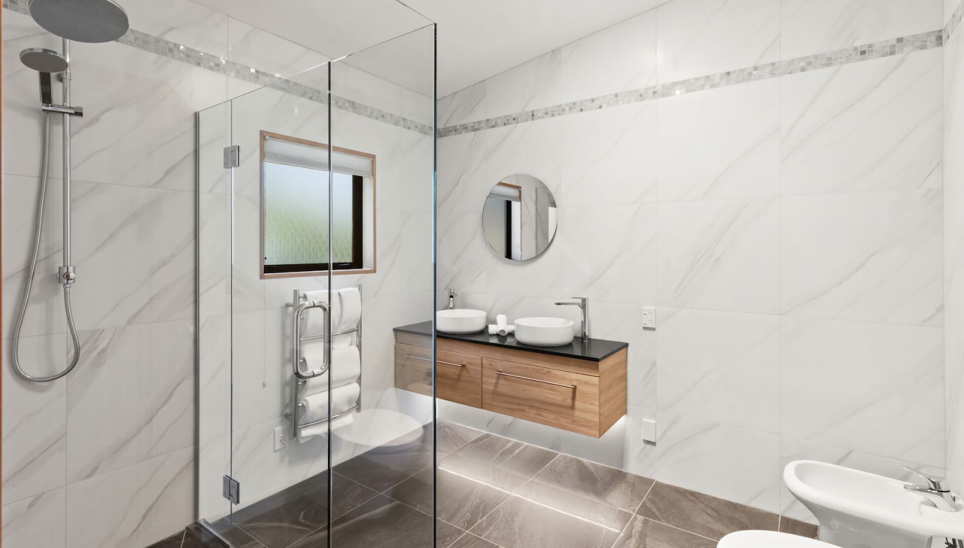 A modern bathroom with a glass shower enclosure, a wooden vanity with two sinks, and a separate toilet area.