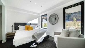 Un dormitorio moderno con una cama grande, un sofá, un espejo redondo y vistas al exterior.