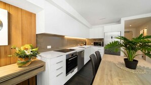 Una cocina moderna con armarios blancos, horno empotrado y un comedor con mesa y sillas de madera.