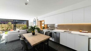 Cocina moderna con armarios blancos, horno empotrado y lavavajillas. Cuenta con un comedor con mesa y sillas, y un ventanal con vistas al jardín trasero.