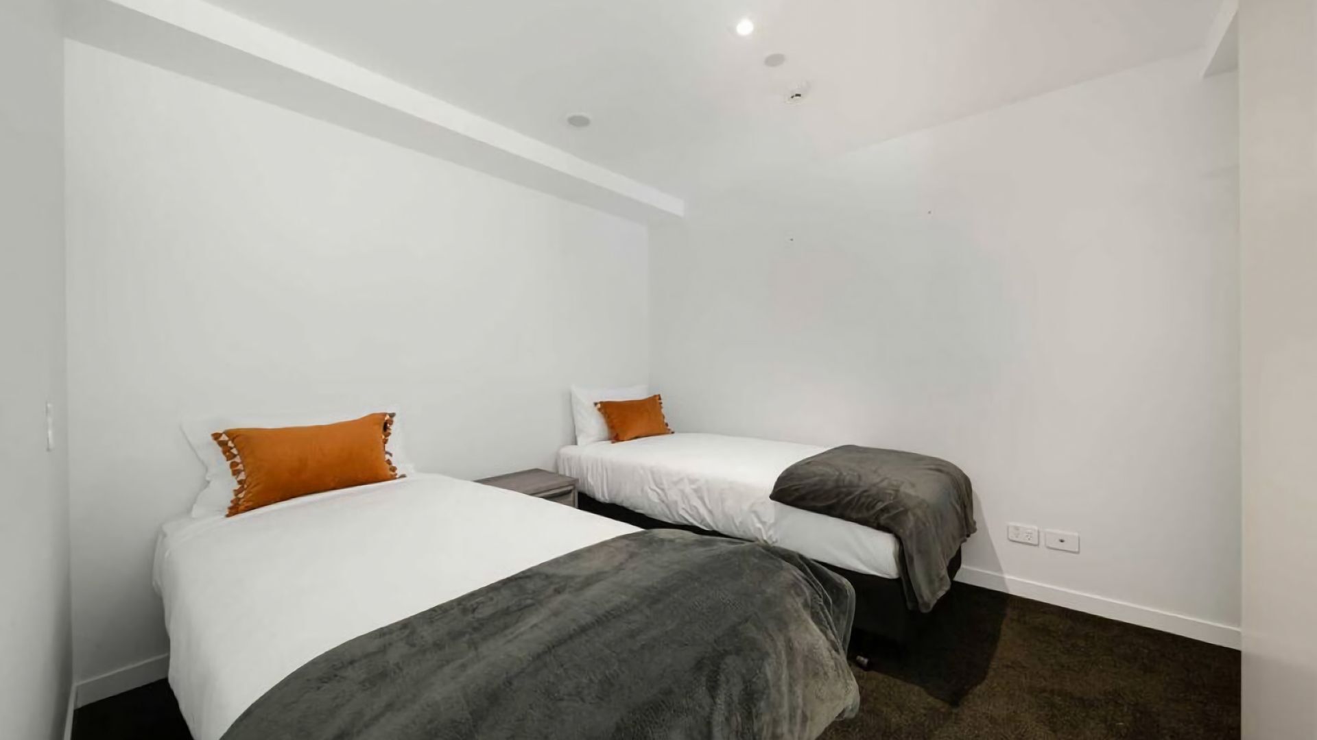 Een kleine, moderne kamer met twee eenpersoonsbedden, witte muren en een donker vloerkleed.