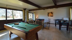 A pool table with a green felt surface, a foosball table, and a billiards table in a room with large windows and wooden beams on the ceiling. - Liege Cottage With Sauna (Waimes)