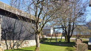 A building with a stone facade and a grassy yard with trees and a swing set. - Liege Cottage With Sauna (Waimes)