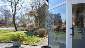 A modern building with a glass door, a small garden with a potted plant, and a wooden structure with baskets and flowers. - Liege Cottage With Sauna (Waimes)