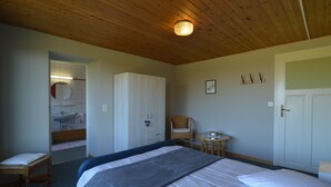 A bedroom with a bed, a chair, a small table, a wardrobe, and a bathroom visible through an open door. - Liege Cottage With Sauna (Waimes)