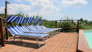 A wooden deck with blue-striped lounge chairs and a pool. - Belvilla by OYO Montebello Mono C (Bolano)