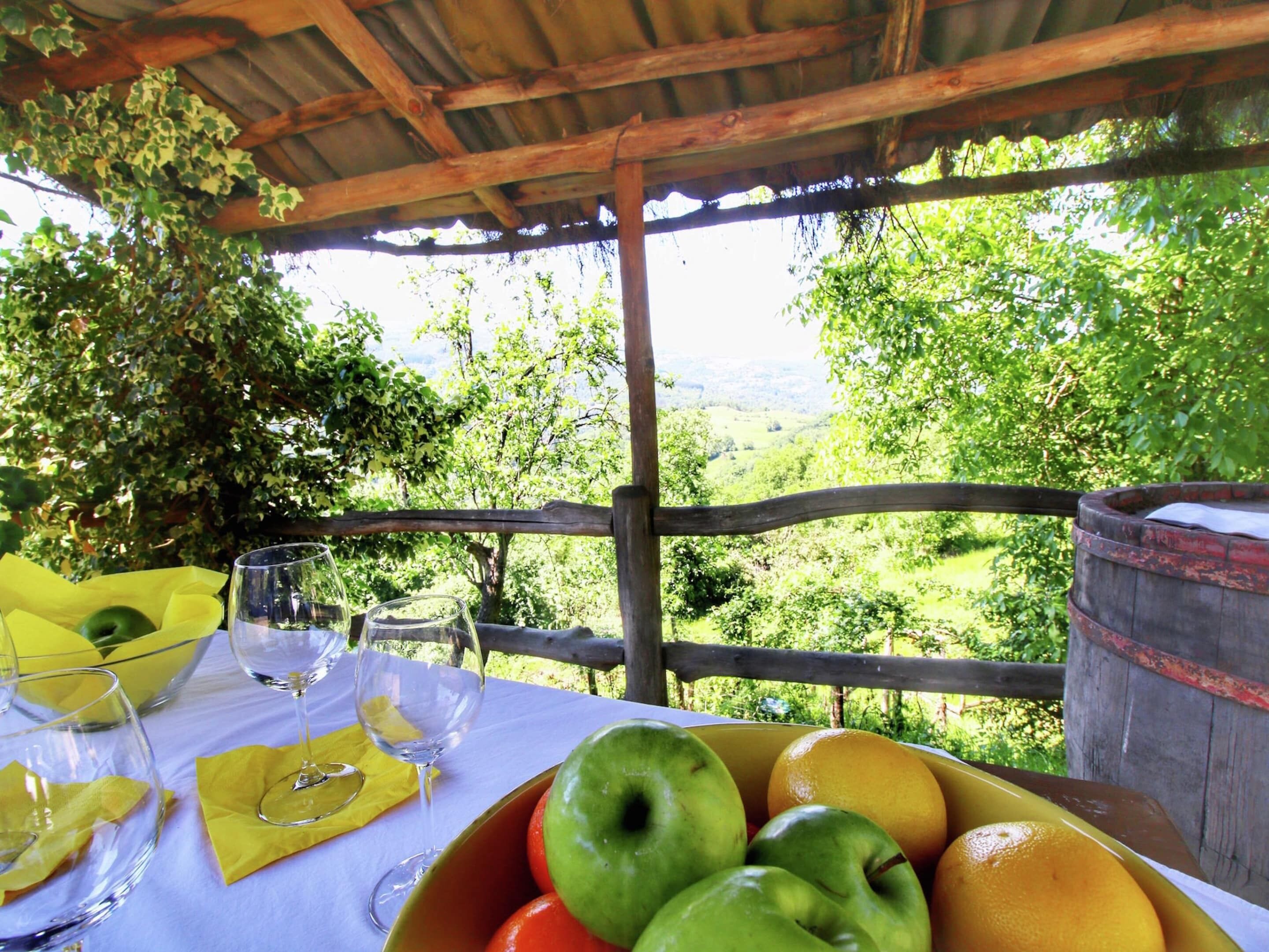 A table with a white tablecloth, a bowl of fruit, and two wine glasses.