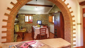 A dining area with a stone wall, a wooden table set for two, and a television on a stone wall. - Charming Tuscan Farmhouse (Ortignano Raggiolo)