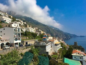 A coastal town with buildings on a hillside, a road with parked cars, and a clear view of the sea. - Apartment near Praia with Large Terrace & Spectacular Views (Praiano)