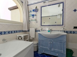 A bathroom with a white bathtub, a blue vanity with a mirror, and a small white stool. - Apartment near Praia with Large Terrace & Spectacular Views (Praiano)