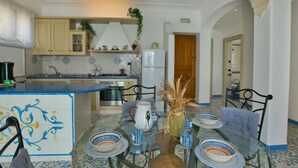 A modern kitchen with a central island, a dining area with a glass table, and a living space with a sofa and a TV. - Apartment near Praia with Large Terrace & Spectacular Views (Praiano)