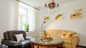 A living room with a leather sofa, a round wooden coffee table, a potted plant, and a window with curtains. - Farm With Lovely Panoramic Views (Trois-Ponts)