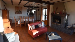 A cozy living room with a fireplace, a dining area with chairs, and a kitchen in the background. - Apartment in Belgium Near Scenic Trails (Malmedy)