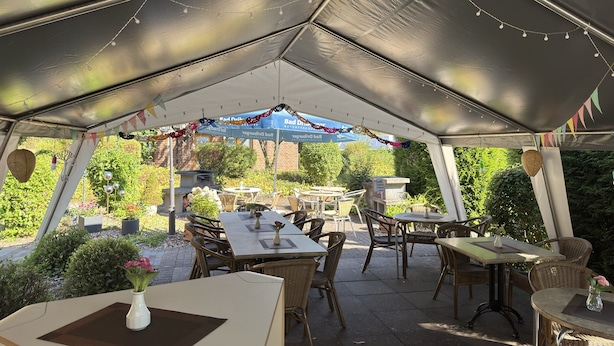 Un espace extérieur aménagé en terrasse, avec des tables et des chaises, un barbecue et des guirlandes lumineuses.