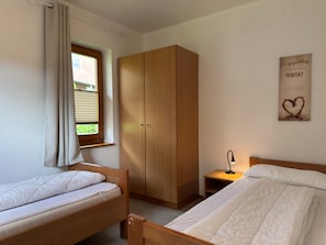 A bedroom with two single beds, a wardrobe, a bedside table with a lamp, and a window with curtains. - Holiday Apartment in the Naturpur Holiday Village (Brakel)