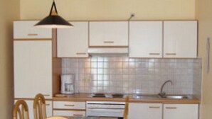 A compact kitchen with white cabinets, a wooden dining table, and chairs. - Holiday Home in Germany With Terrace (Brakel)