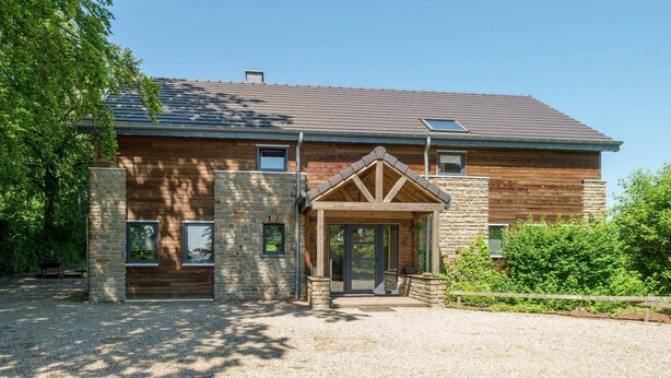 Une maison en rondins de style moderne, avec des fondations en pierre, un toit en pente et une véranda à l’avant.