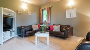 Un salon avec un téléviseur, deux canapés en cuir, une table basse blanche et une fenêtre avec des rideaux.
