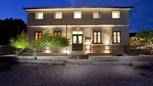 A two-story building with a symmetrical facade, a central entrance with a door, and multiple windows. - Attractive Villa With Private Swimming Pool, Beach Volleyball and Fenced Garden (Rasa)