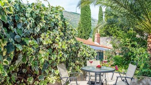 An outdoor patio with a round table and chairs, surrounded by lush greenery and a stone wall. - Dubrovnik Coastal Gem (Dubrovnik)