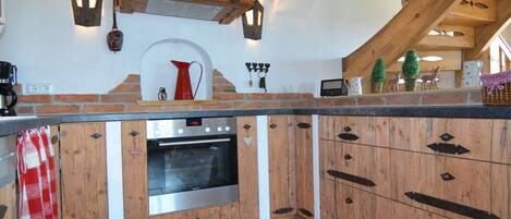 A kitchen with a brick wall, wooden cabinets, a built-in oven, and a shelf with red mugs.
