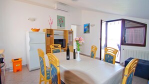 Un coin repas comprenant une table, des chaises, un réfrigérateur, un téléviseur et une fenêtre avec des rideaux.