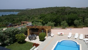 Un espace aménagé au bord de la piscine, avec un barbecue, des chaises longues et une vue sur la mer.