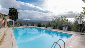 Une piscine à l’eau d’un bleu cristallin, entourée de chaises longues et de parasols, avec une vue sur les montagnes en arrière-plan.