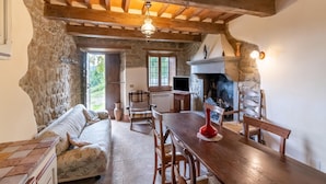 Un intérieur rustique avec des poutres apparentes, un mur en pierre, une cheminée, une table à manger et un canapé.