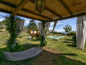 A covered outdoor area with a pool, a lounge chair, and a small building in the background. - Belvilla by OYO Casaletto Graffi (Graffignano)