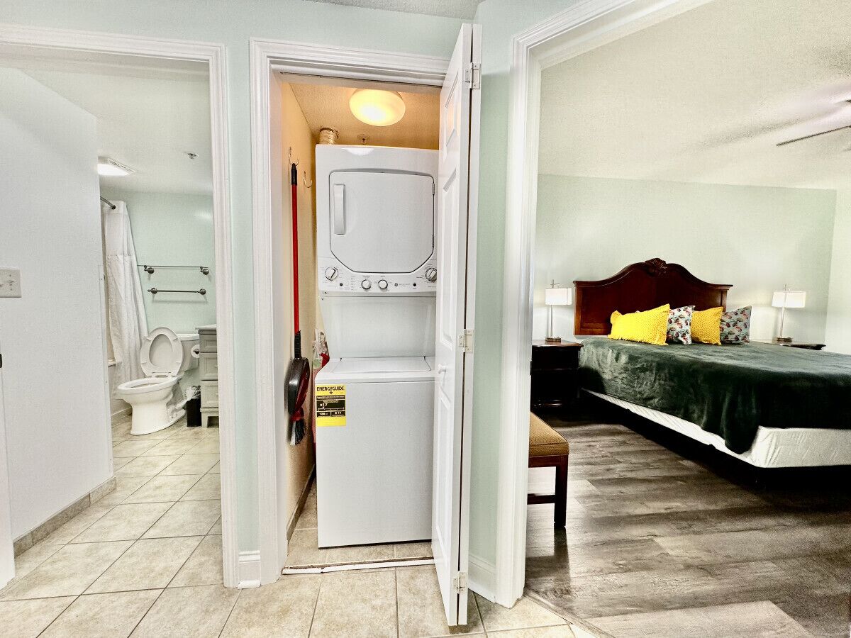 Une chambre d’hôtel comprenant un lit, une petite table, un lave-linge et une salle de bain avec des toilettes et une douche.