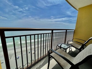 A balcony with a view of the beach, equipped with two chairs and a small table.