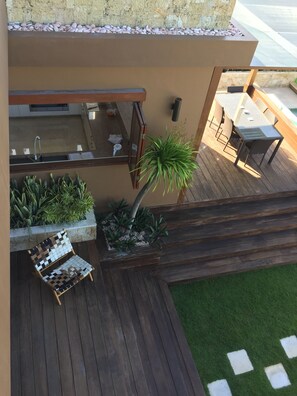 Une terrasse dotée d’un barbecue intégré, de coins salon extérieurs et de jardinières contenant diverses plantes.
