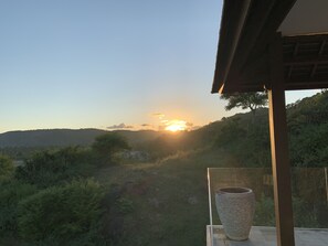 Un balcon offrant une vue sur un coucher de soleil se déclinant sur un paysage vallonné.