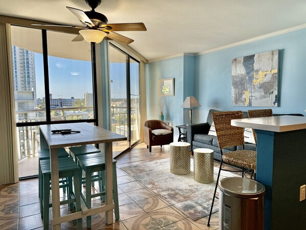 Una sala de estar moderna con comedor, ventanas grandes, ventilador de techo y vista de la ciudad.