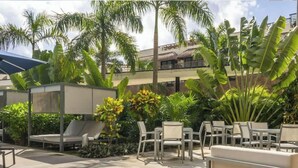 Un patio de hotel con mobiliario exterior, palmeras y un edificio al fondo.