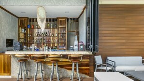 Zona de bar con estantes de madera llenos de botellas, una barra con taburetes y un sofá blanco.