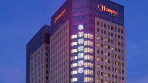 A high-rise hotel with a prominent "Hampton" sign, multiple floors, and a modern glass facade. - Hampton BY Hilton Yangzhou Slender (Yangzhou)