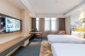 Une chambre d’hôtel avec un lit, un bureau, une chaise, une télévision et une fenêtre avec des rideaux.
